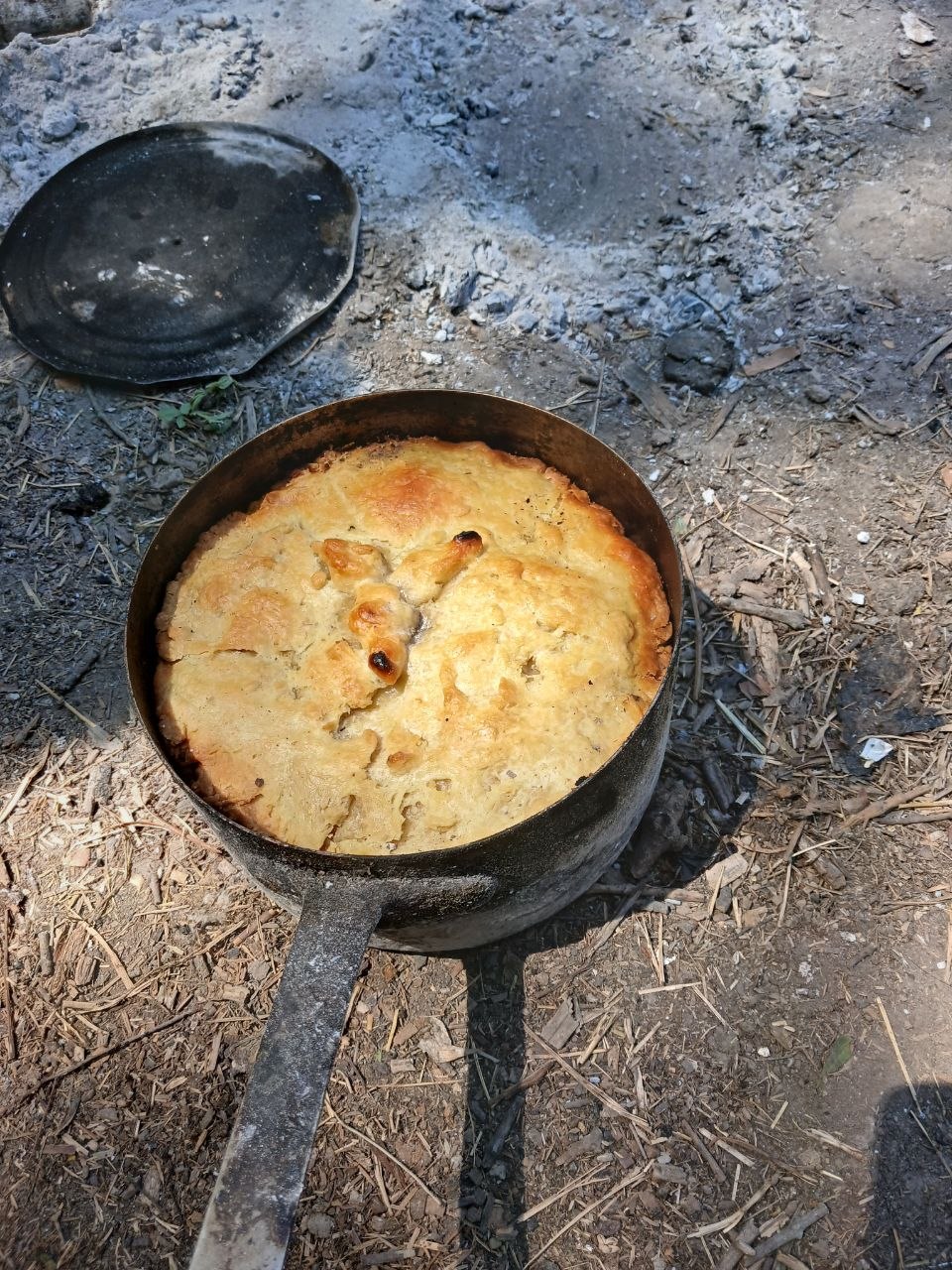 Un pâté en croûte doré, cuit dans une cocotte en fonte posée sur les cendres